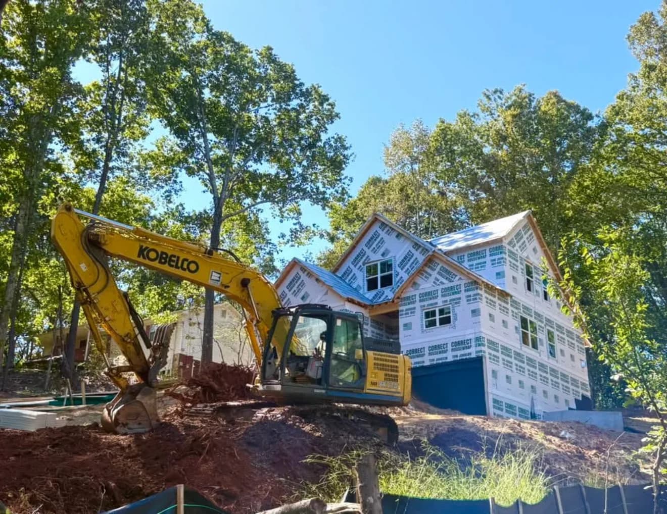 Excavator grading the lot beside a house being rebuilt
