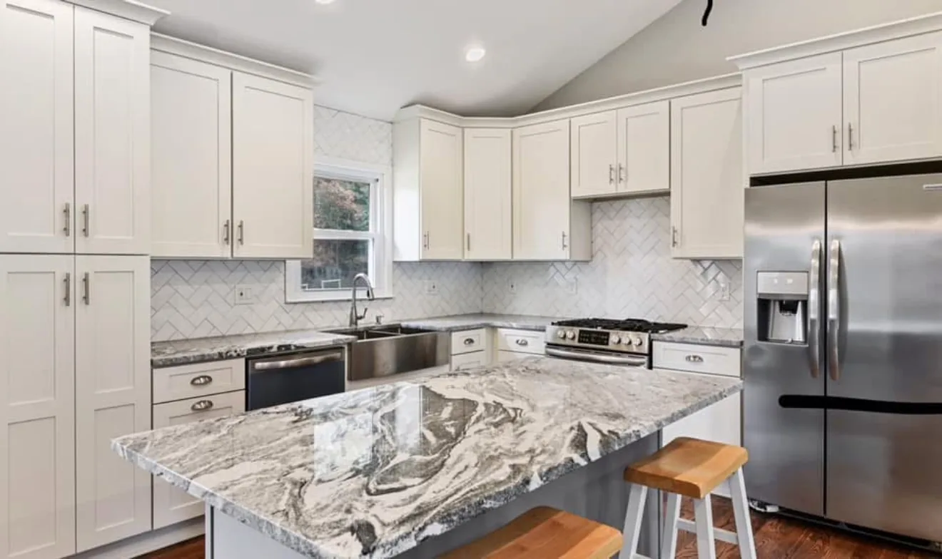 Renovated kitchen with a waterfall granite island, white cabinetry, and stainless appliances