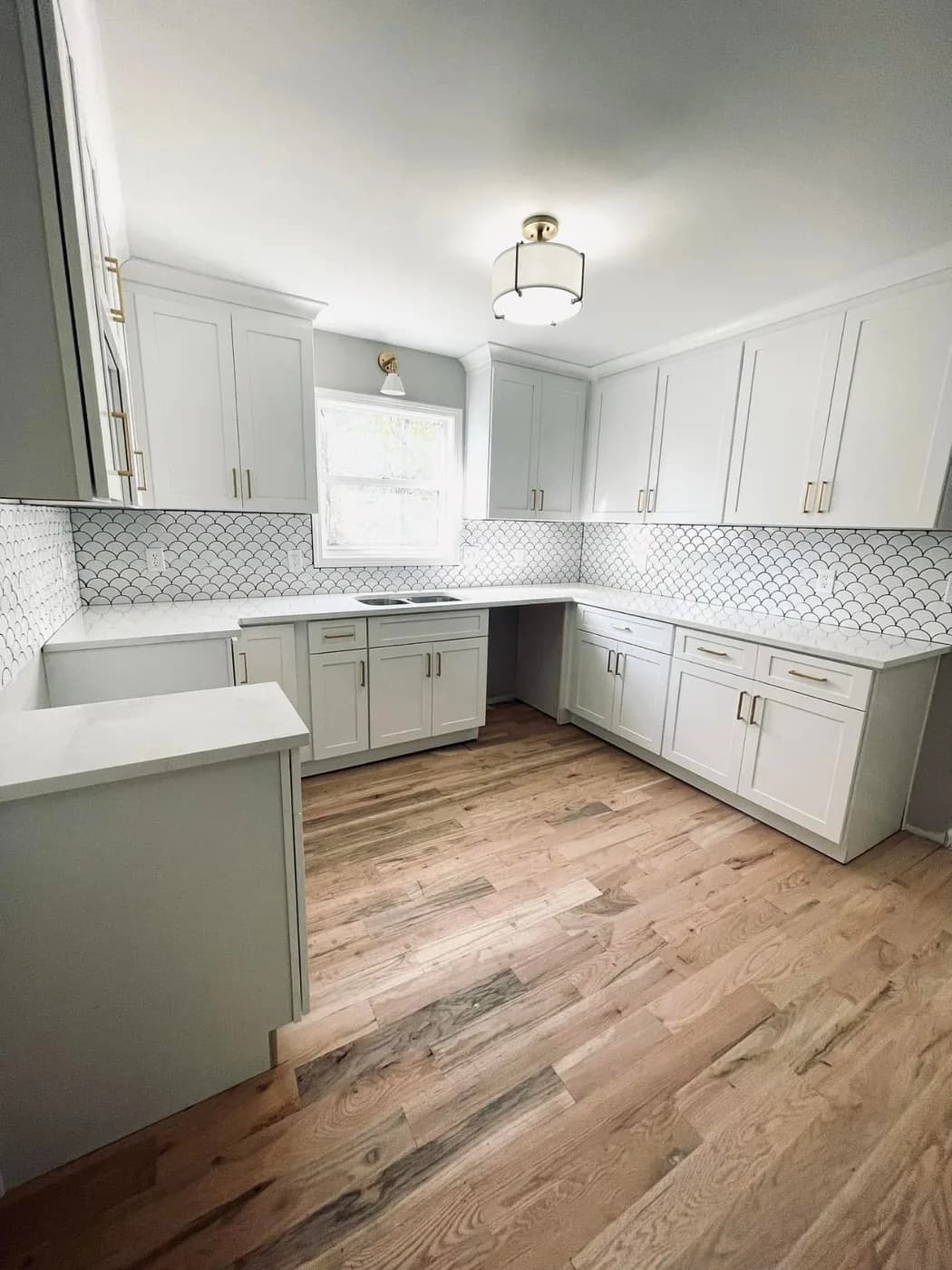 White shaker kitchen with a geometric tile backsplash and wide-plank wood floors