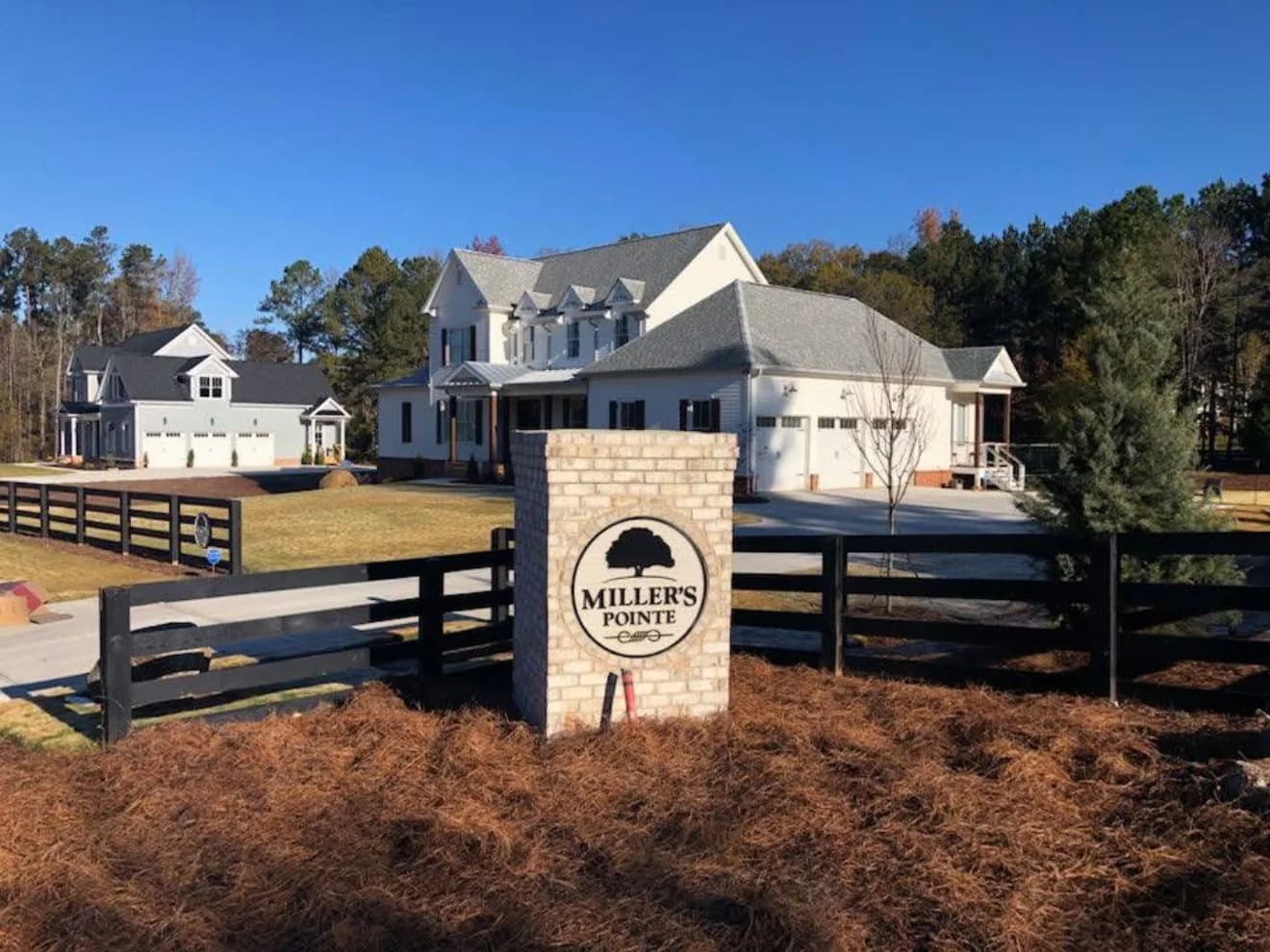 Stone entry monument reading Miller's Pointe with new homes and black fencing behind it