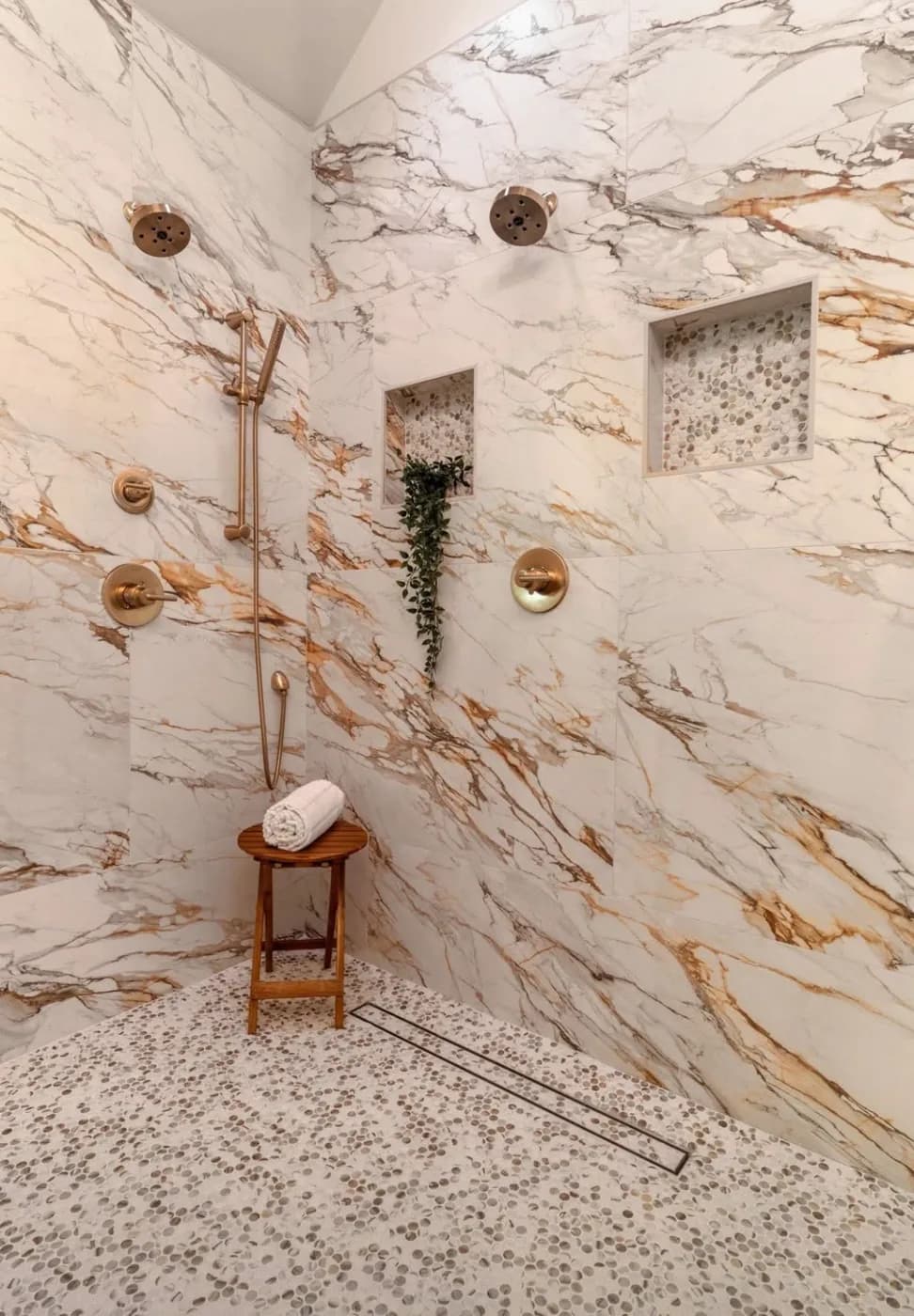 Walk-in shower clad floor to ceiling in veined marble with brushed gold fixtures